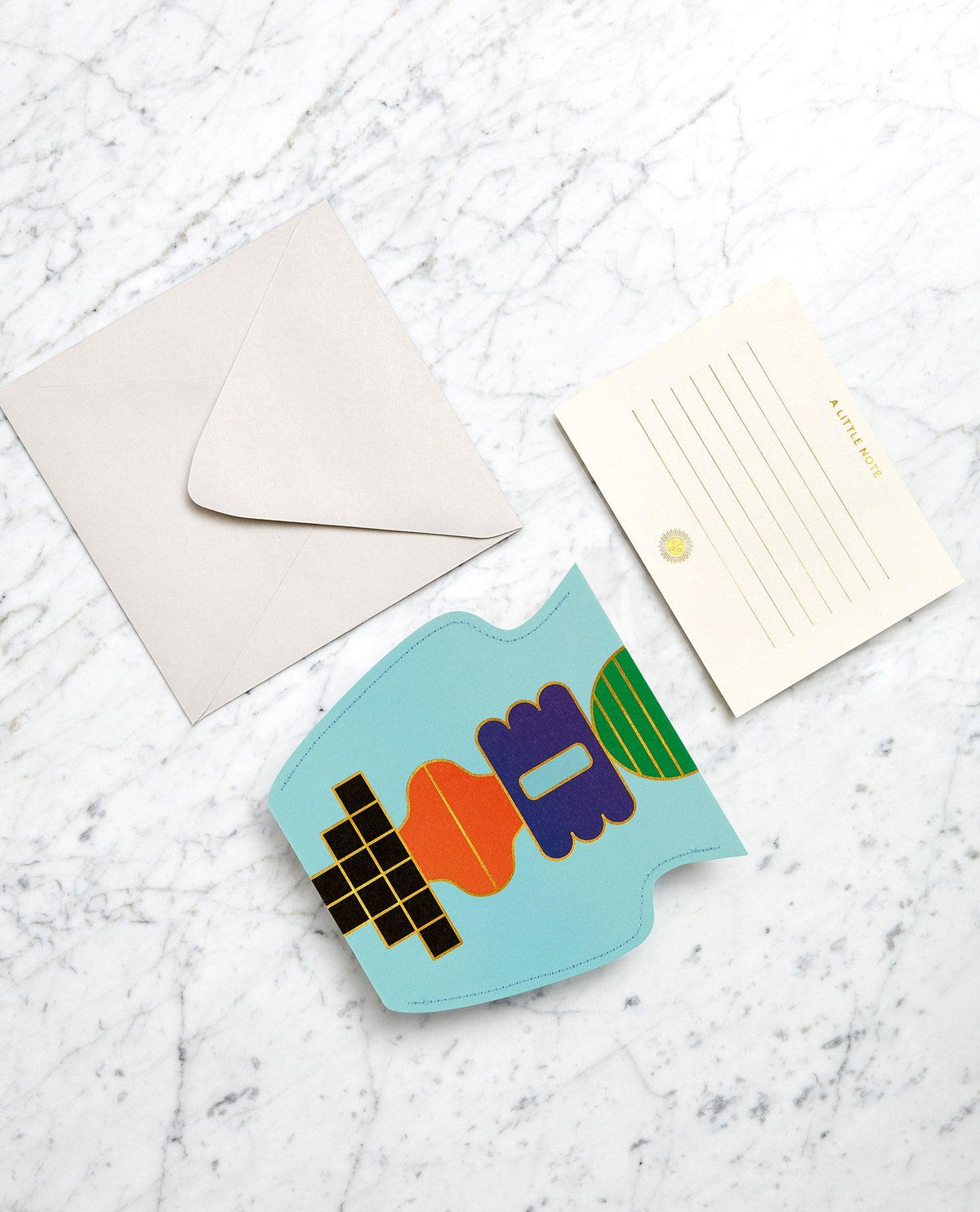 A gold-lined notecard with envelope paired with light blue OCTAEVO Templo Paper Vase on white marble.