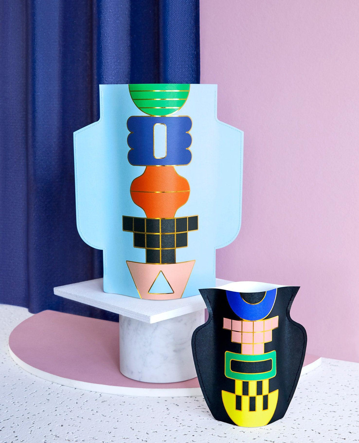 Two Templo Paper Vases by OCTAEVO sit on modern surfaces with pink, light blue, and white Mediterranean-inspired backgrounds.