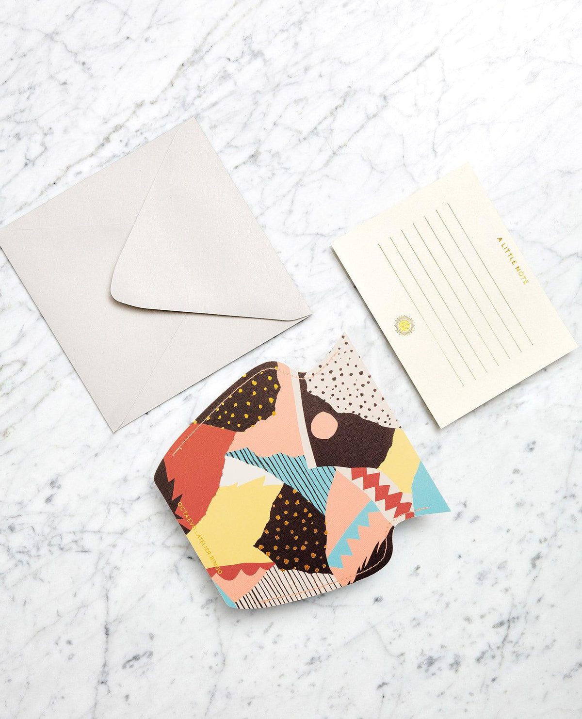 OCTAEVO Vesuvio Mini Paper Vase with abstract design beside gold-lined note card and blank envelope on marble.