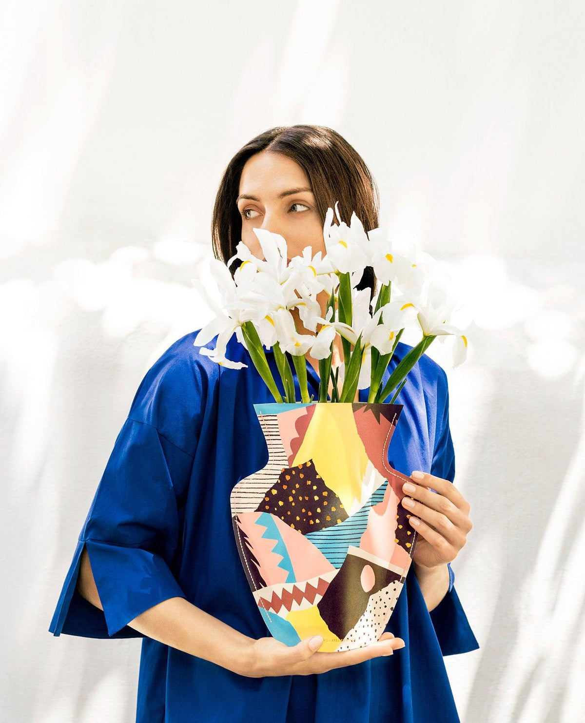 A woman in blue holds OCTAEVO’s Vesuvio Paper Vase with white irises against a light background—a unique gift.